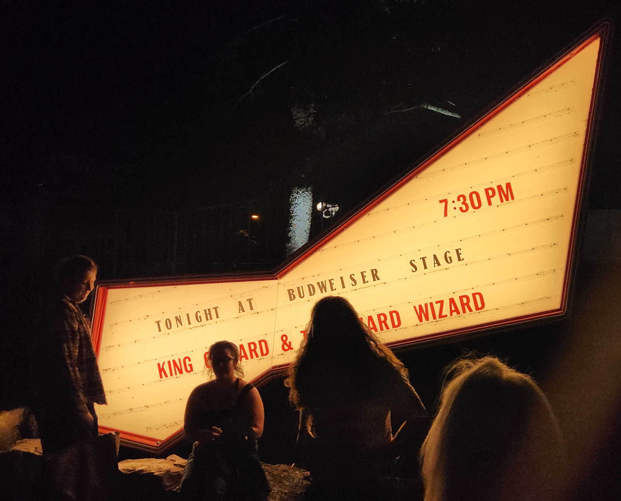 photo of three people in front of an illuminated Budweiser sign announcing the King Gizzard show in Toronto.